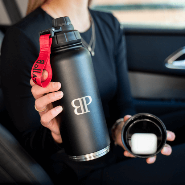 „Bollaz Thermoshaker mit geöffnetem Quickslot-Fach – schwarze Edelstahlflasche mit rotem Strap im Auto, zeigt das praktische Zusatzfach.